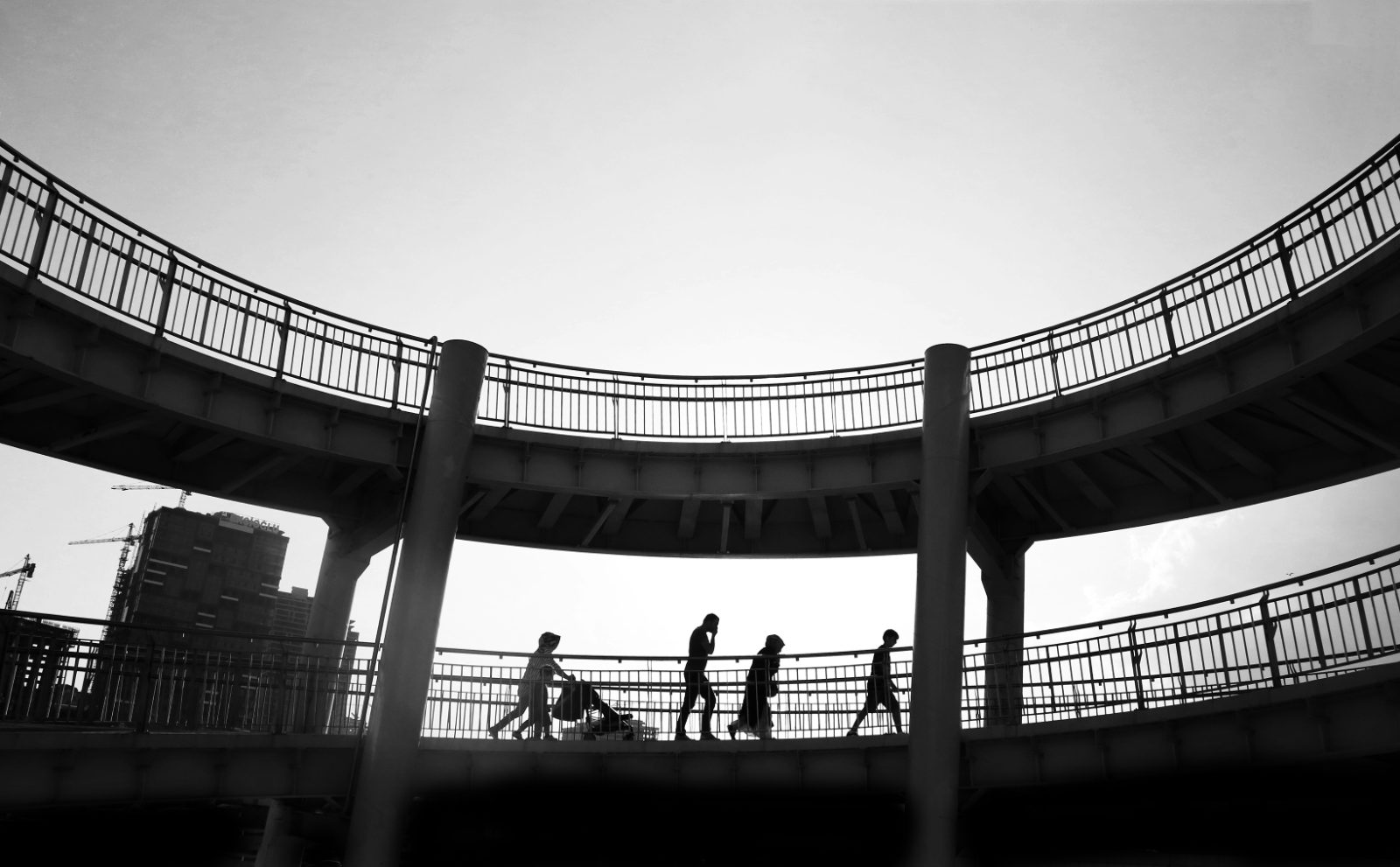 People crossing a curved footbridge, in silhouette